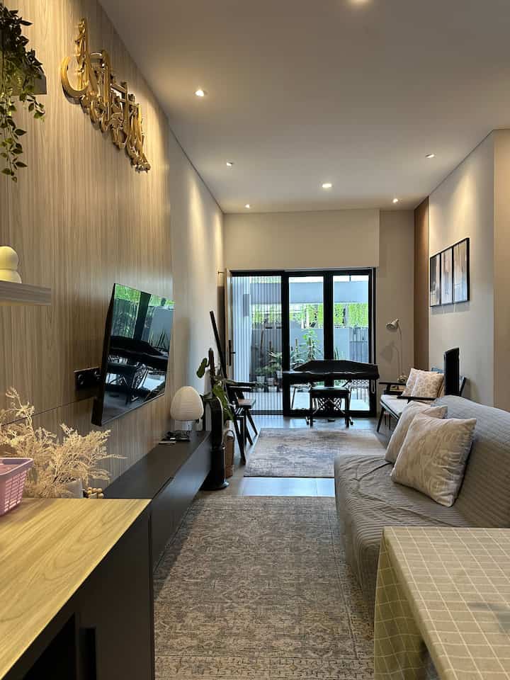 Natural modern narrow living room featuring gray sofa, brown wood paneled wall, and patterned carpets with cozy atmosphere
