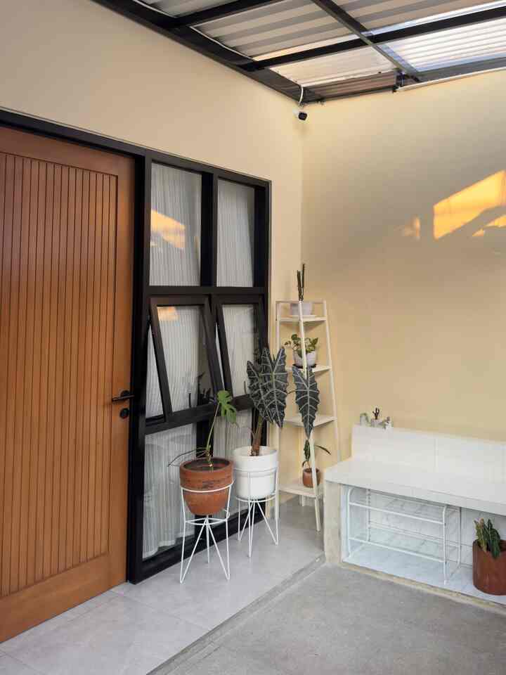 Beige-walled entrance featuring wood-tone door, white plant stands and a tiled bench, creating a natural and cozy atmosphere