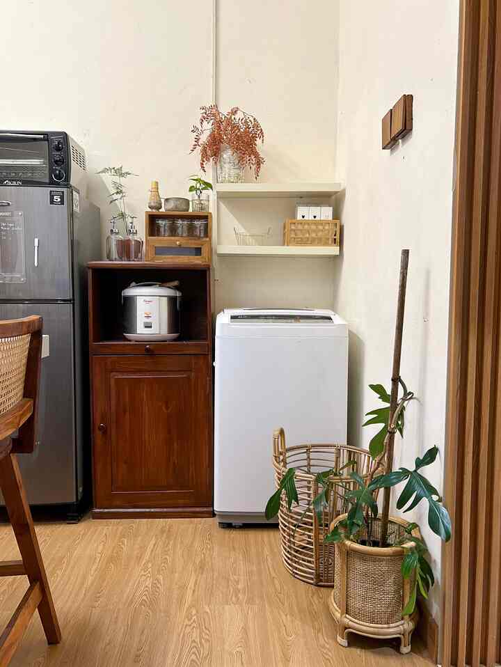 White-walled, wood-toned narrow laundry room featuring a rattan basket, plants, and wooden cabinet creating a cozy atmosphere