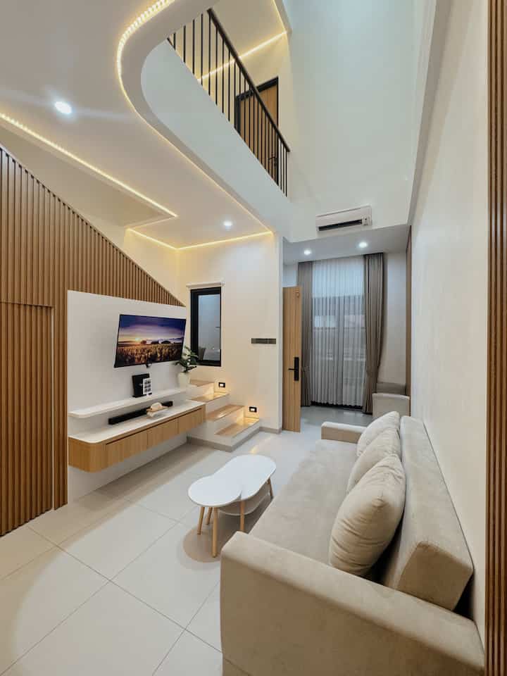 Modern living room with white walls and wood tone accents, featuring a beige sofa bed and coffee table in a clean layout