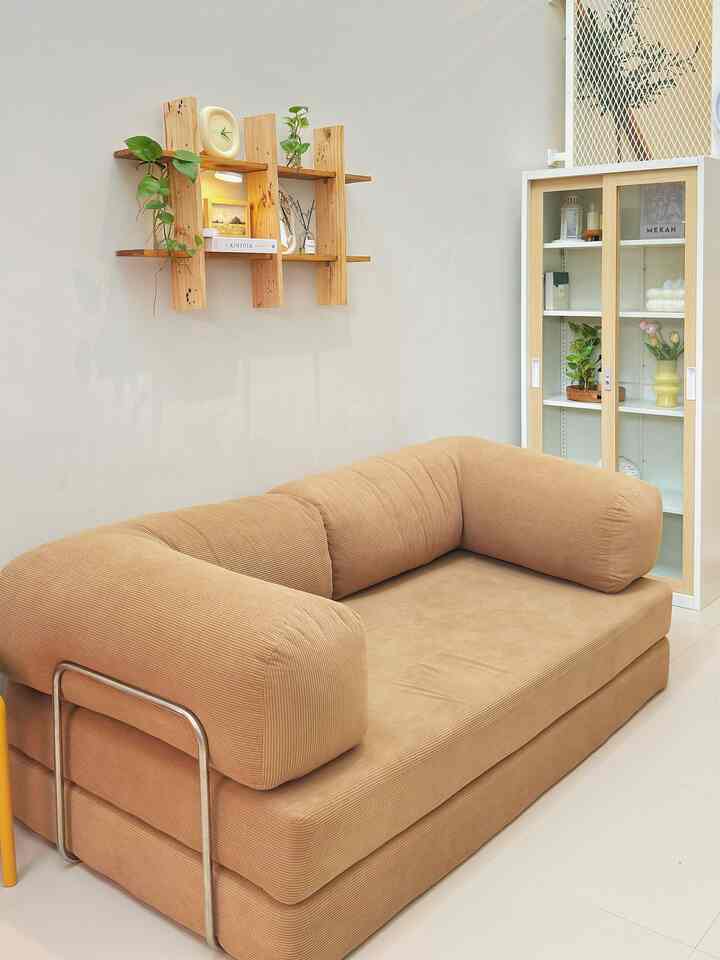 Warm beige-toned living room featuring a beige sofa bed, natural wooden shelves, and plants arranged for a cozy atmosphere