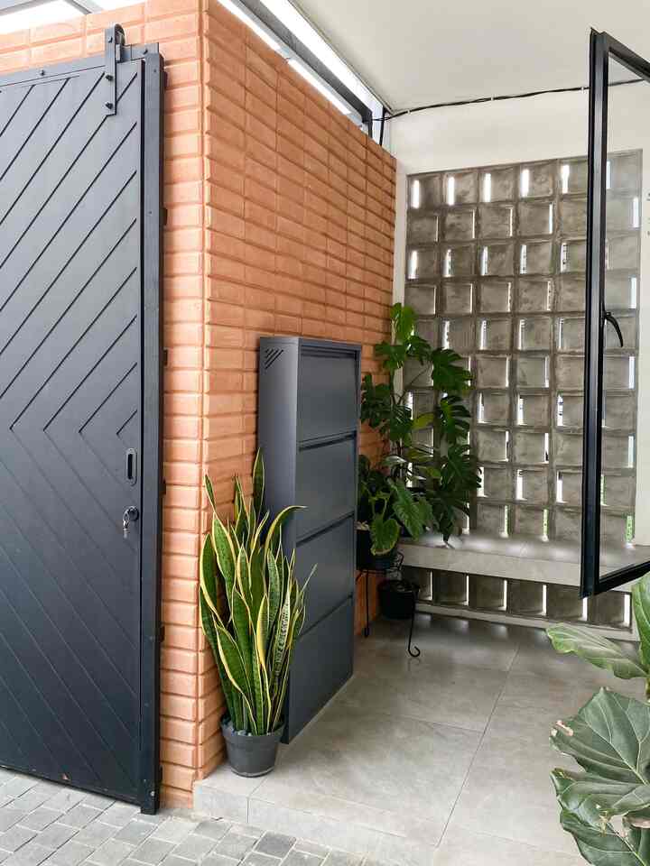 Entrance with brown brick wall, black metal door, and green plants arranged neatly