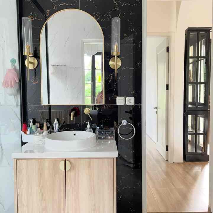White and gold bathroom space featuring a natural wood vanity and wall sconces with modern interior style