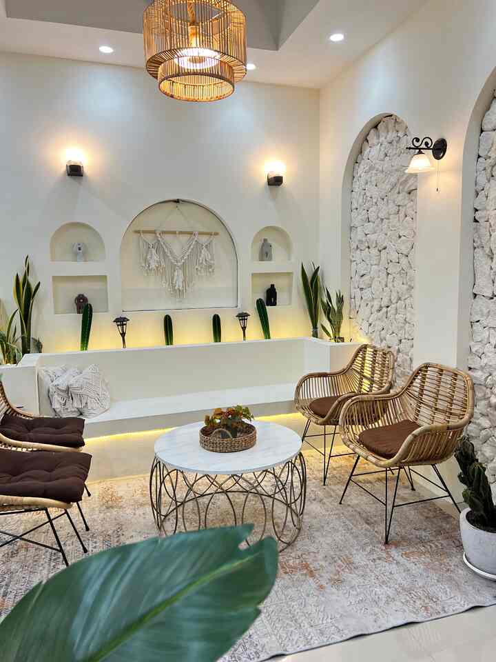Soft natural-toned living room featuring rattan armchairs, white built-in bench sofa, and lush indoor plants creating a cozy atmosphere