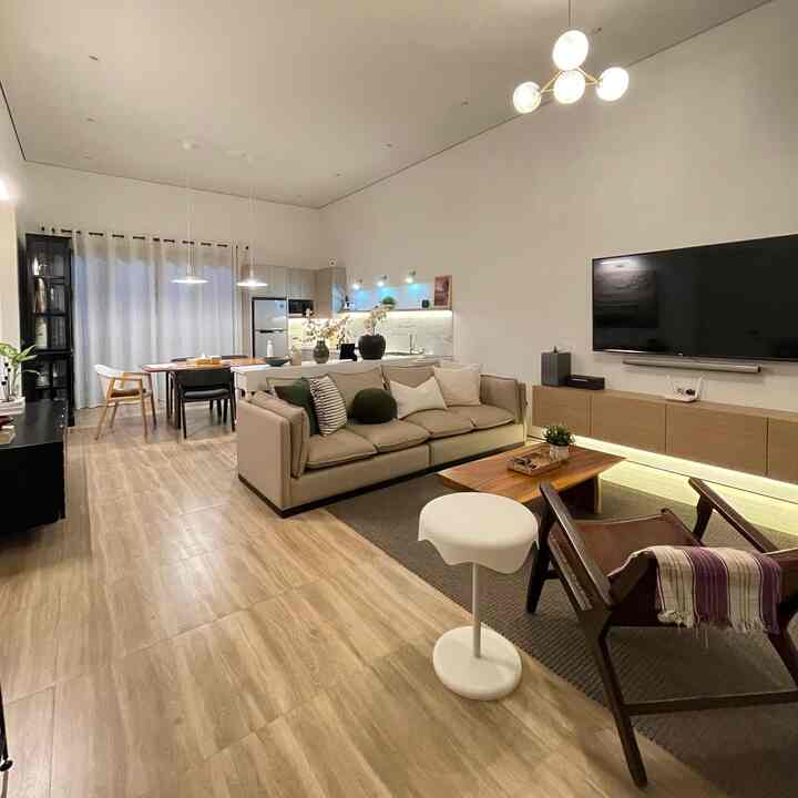 Modern living room and kitchen featuring beige and wood tones, with a console table and pendant lighting arranged in a clean interior