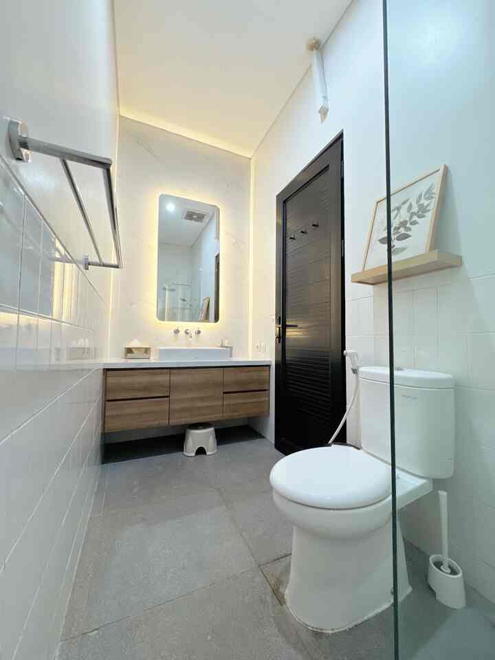 Modern bathroom in white and brown tones featuring a floating wooden vanity, soft LED-lit mirror, and a sleek black door with clean aesthetic
