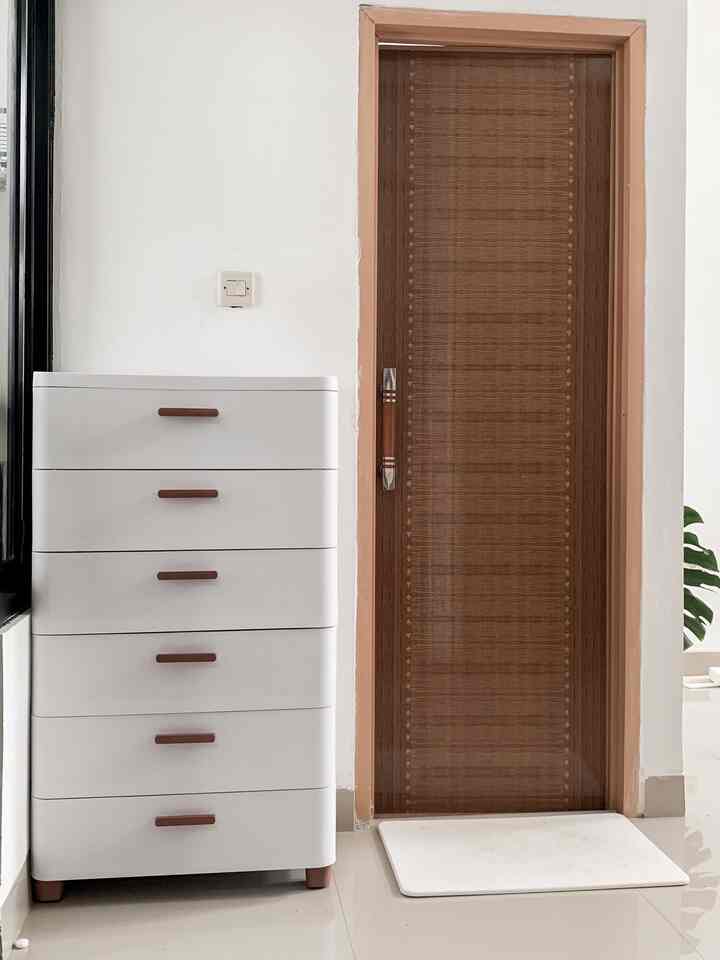White and brown toned bathroom featuring a white storage cabinet, wooden door, and bath mat with a clean interior
