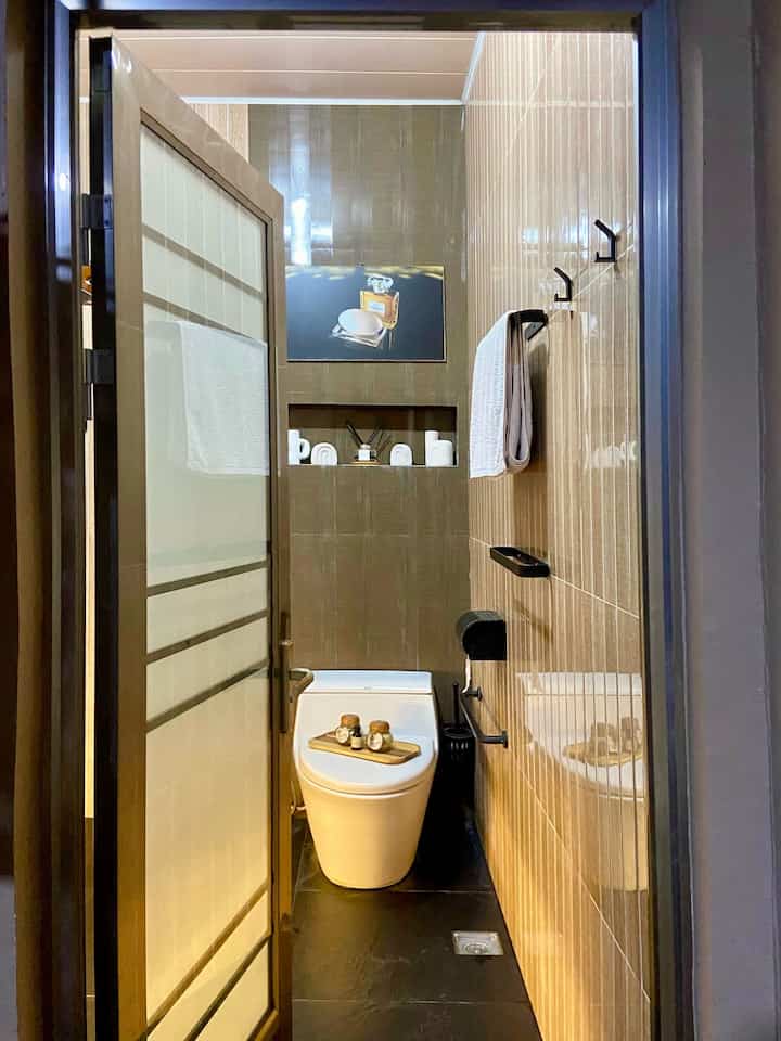 A narrow modern restroom featuring brown tiled walls and black floor tiles, with a sleek high-tech toilet centered neatly
