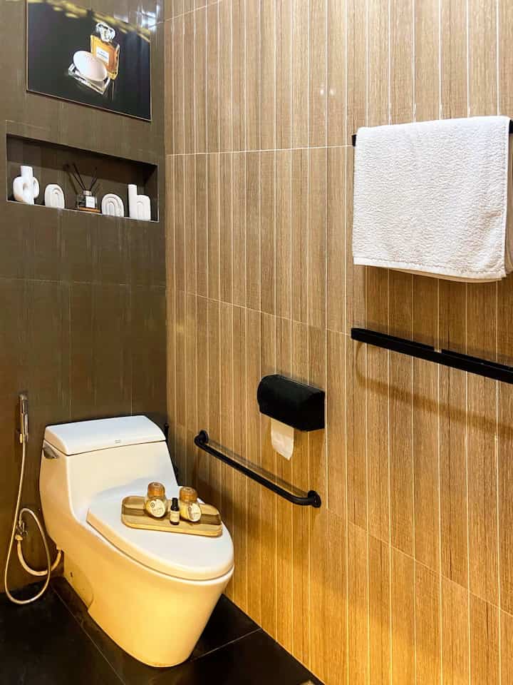 Modern bathroom space with brown and black tones featuring a central white toilet and towel rack on the wall, neat and clean design