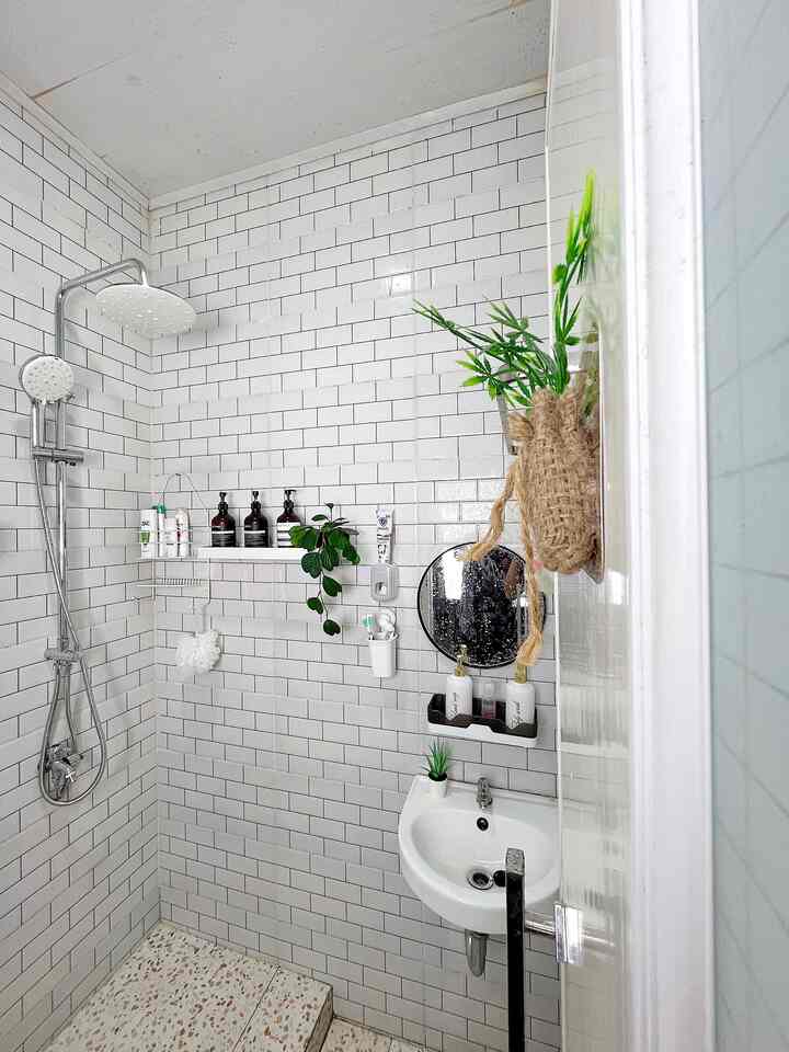 White tiled bathroom featuring a small sink, round mirror, and green plants creating a cozy atmosphere