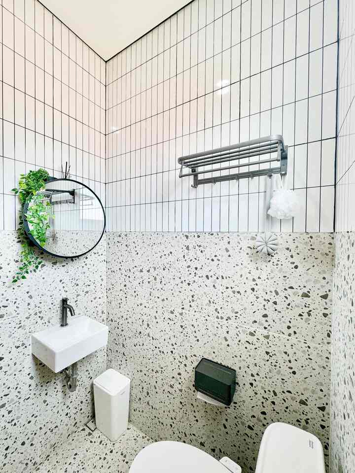 White tiled bathroom with terrazzo walls featuring round mirror and small sink, creating a minimal and clean atmosphere
