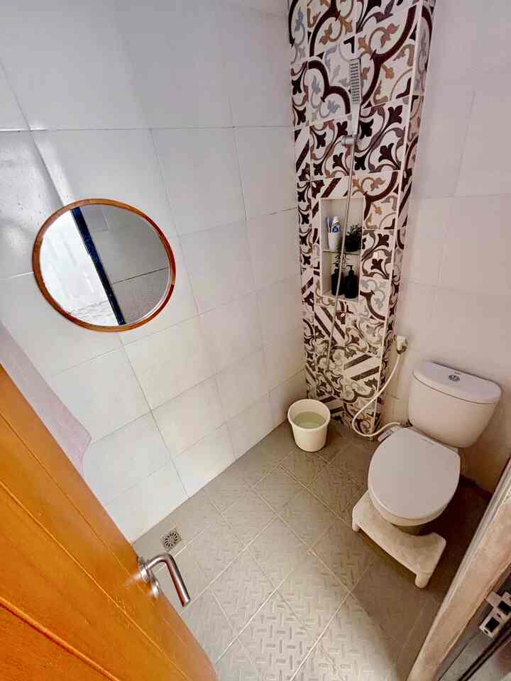 Modern small bathroom with light gray tiles and patterned accent wall, featuring a round mirror and vertical storage niche in a neat layout