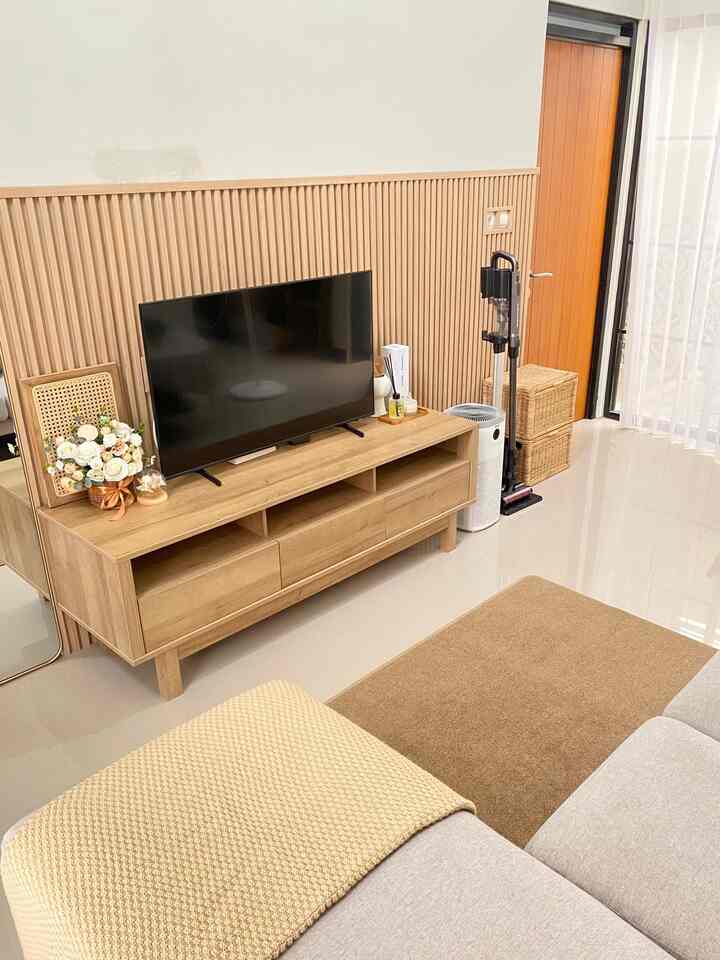 A living room featuring wood tones and beige colors, with a TV stand, gray sofa, and beige blanket creating a cozy atmosphere
