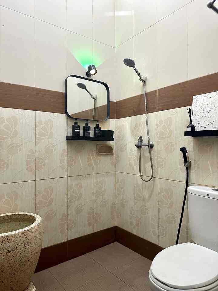 A clean bathroom in white and brown tones featuring a black-framed mirror, showerhead, toilet, and bathroom accessories neatly arranged