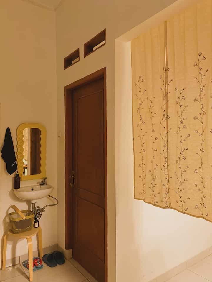 Beige and brown toned entrance featuring a wall-mounted sink, floral curtains, and a wooden stool creating a cozy atmosphere