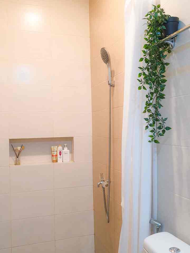Bathroom with white and natural tones, featuring a shower, white curtain, built-in wall shelf with products, and hanging plant for a clean look