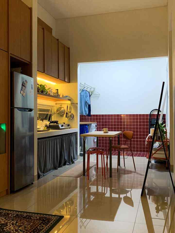 Narrow long kitchen space with red tiled wall and wood-tone cabinetry, featuring a dining table and chairs for a warm ambiance