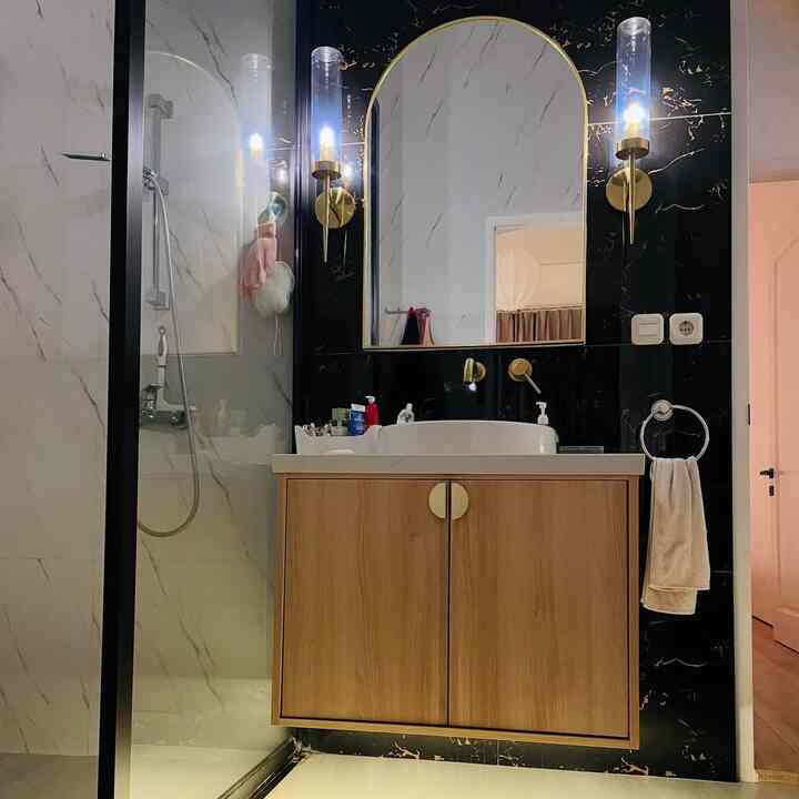Modern luxurious bathroom featuring black marble walls with a wooden vanity and gold bronze wall sconces