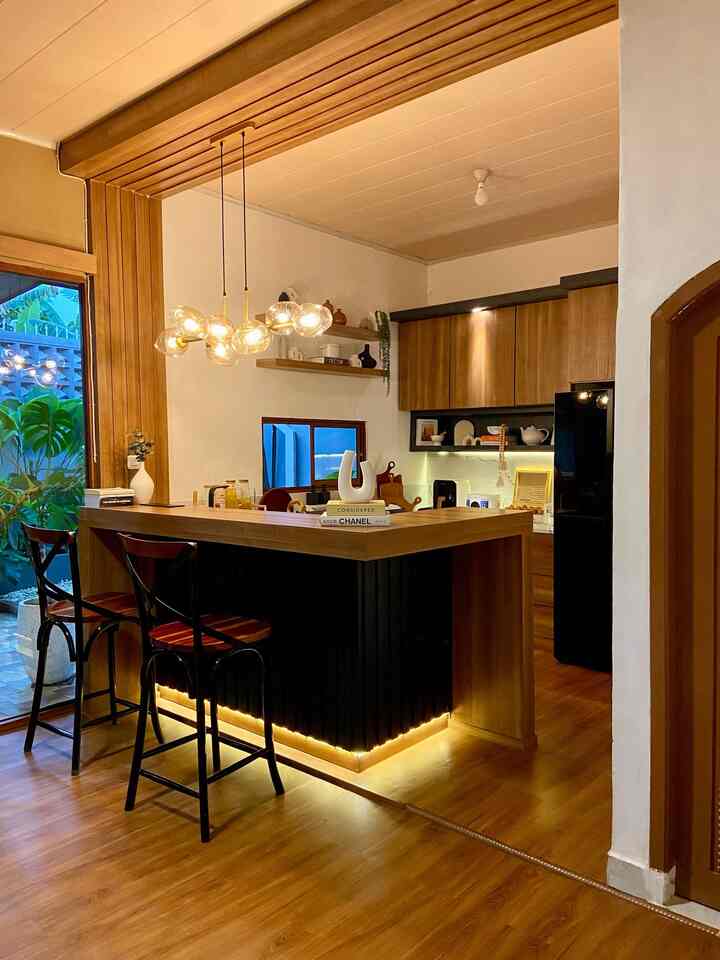 Warm wood tones and black accents define this kitchen space featuring an island dining table and pendant lighting for a modern cozy home cafe atmosphere