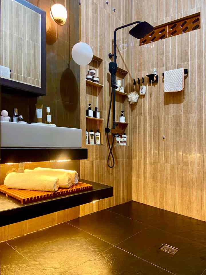 A warm brown-toned bathroom featuring gold lighting accents, a neatly arranged wash basin and shower shelves in a modern setting