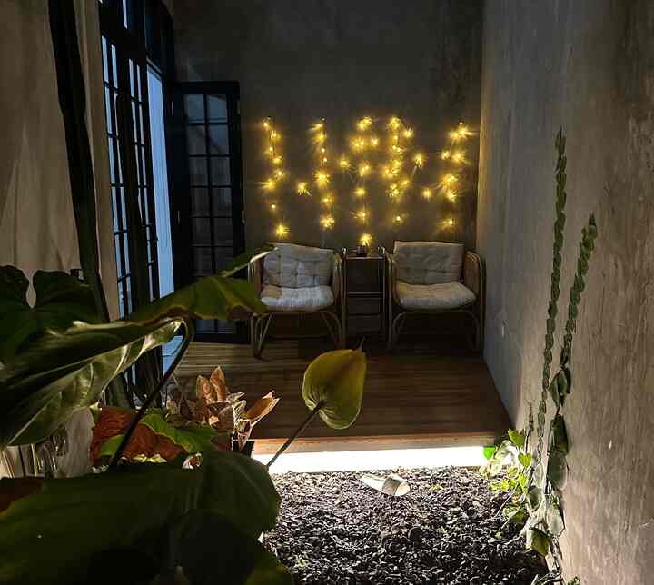 Natural modern living space with dark gray walls, brown wood tone flooring, two rattan armchairs, and yellow string lights