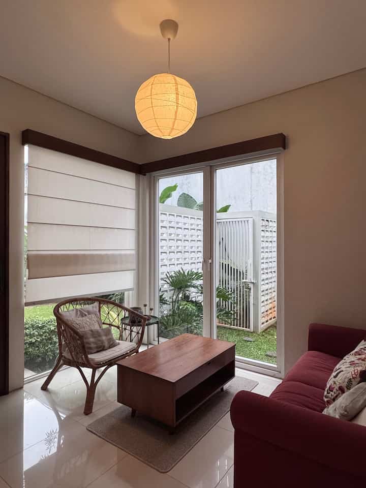 Beige-toned small living room with plum sofa and rattan armchair in cozy natural modern interior