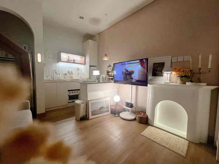 Warm beige-toned living room and kitchen space featuring TV and various table lamps creating a cozy atmosphere