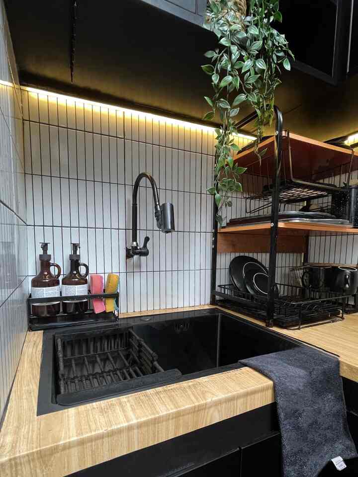 Modern kitchen in black and wood tones featuring a black sink and faucet, hanging plant, and dish rack