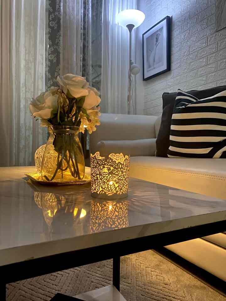 White-toned living room featuring a white leather sofa, flower vase, and warm lighting creating cozy ambiance