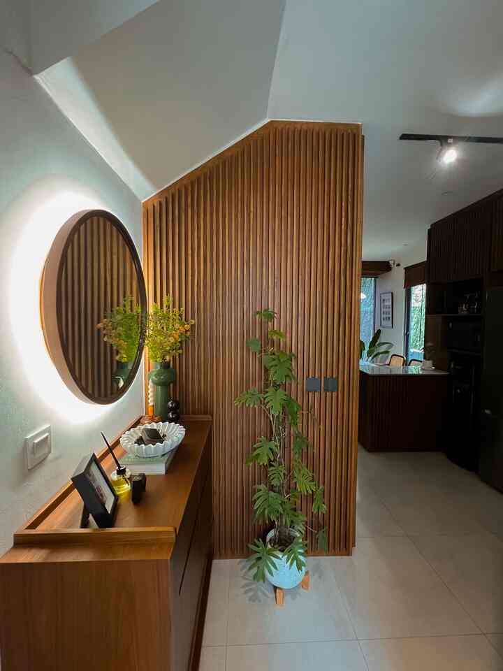 Begitu buka pintu, langsung disambut area ini. Yes, foyer ini memang kami rancang sebagai titik awal yang ngasih vibes hangat & mid-century banget ke tamu yang datang (dan juga buat kami sendiri setiap pulang ke rumah).

✨ Dinding wooden slat sengaja dibuat menonjol — bukan cuma sebagai statement visual, tapi juga untuk nambah privasi. Jadi, pandangan dari pintu masuk nggak langsung tembus ke ruang keluarga. Lebih tenang, lebih tertata.

✨ Meja ini multifungsi: bukan sekadar konsol, tapi juga sekaligus rak sepatu tersembunyi. Bikin area tetap rapi tanpa mengorbankan fungsi.

✨ Ada cermin bundar backlit buat touch-up cepat sebelum keluar rumah, dan beberapa dekor fungsional seperti mangkuk tempat kunci & diffuser untuk aroma segar.

✨ Jangan lupa juga ada tanaman hijau biar masuk rumah langsung terasa hidup dan adem.

Kami percaya, first impression of a home starts at the entrance — dan area kecil seperti ini bisa jadi tempat yang penuh makna kalau ditata dengan cinta 🤍 #foyer #wallpanel #inspirasifoyer #pintumasuk #inspirasiruangdepan #foyerrumah #midcentury #kayusolid #wallpanelkayu #raksepatu