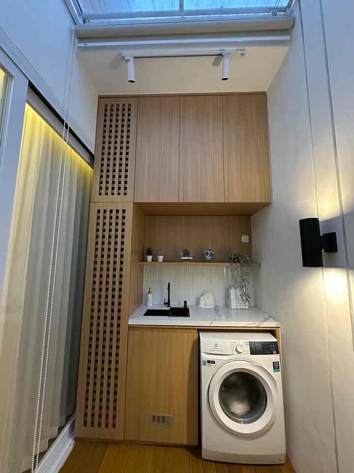 Wood tone and white compact laundry area featuring washing machine and storage cabinets in a neat studio apartment interior