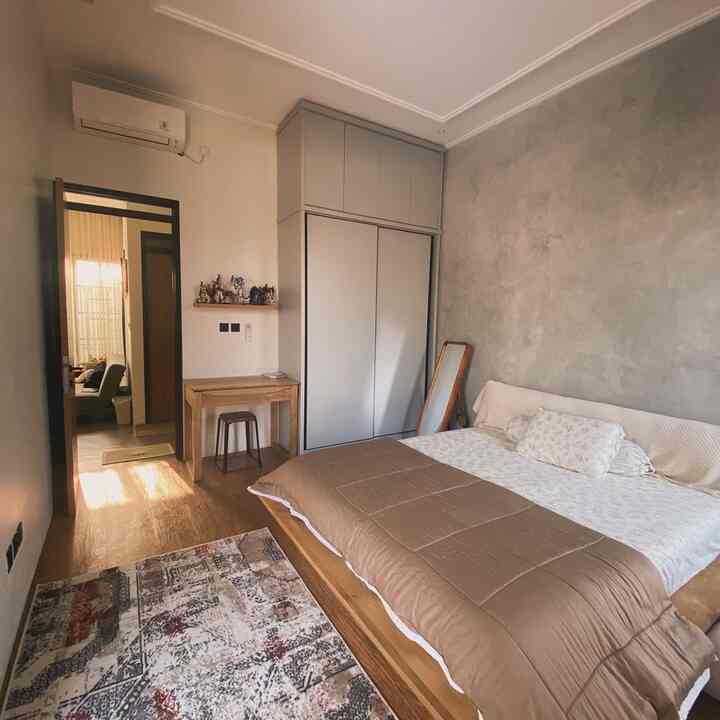 Natural wood tone bedroom featuring a mid-sized bed, patterned carpet, standing mirror, and small desk in a simple layout