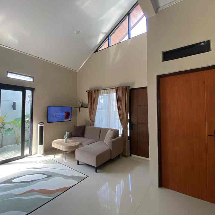 Bright white tiled floor with brown wooden doors, beige sofa, high vaulted ceiling and large windows in a compact living room space