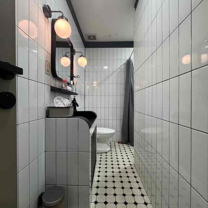 Monotone narrow simple bathroom featuring custom sink, mirror, and warm wall sconces with cozy atmosphere