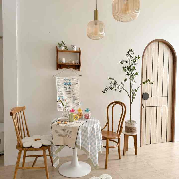 Bright natural-toned dining room near kitchen featuring wooden chairs, white round dining table with colorful accessories in a cozy cafe style