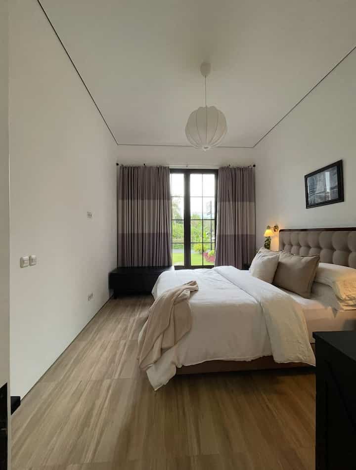 White and wood tone bedroom featuring central bed and pendant light with a clean, cozy atmosphere