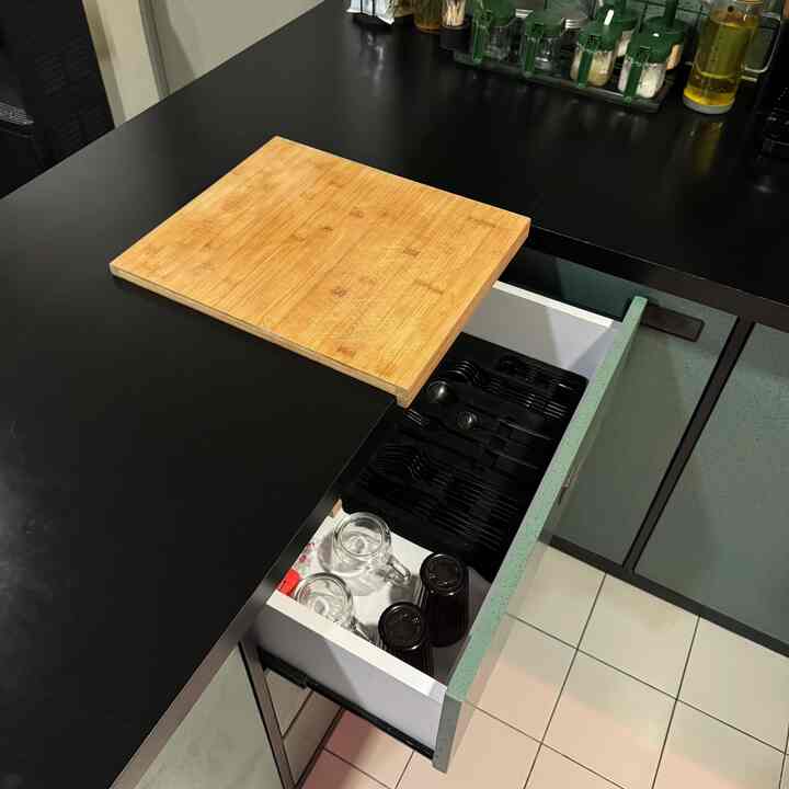 Black kitchen countertop featuring a wood tone cutting board and organized cutlery drawer in a clean kitchen space
