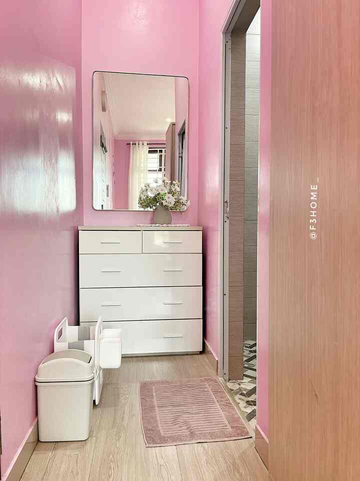 Bright pink walls define a narrow entrance space featuring a white dresser, pink mat, and trash bins near the doorway