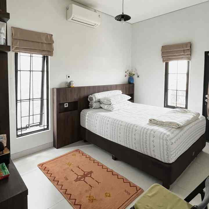 Cozy bedroom with white walls and brown bed frame, featuring a small pink carpet and minimal furniture