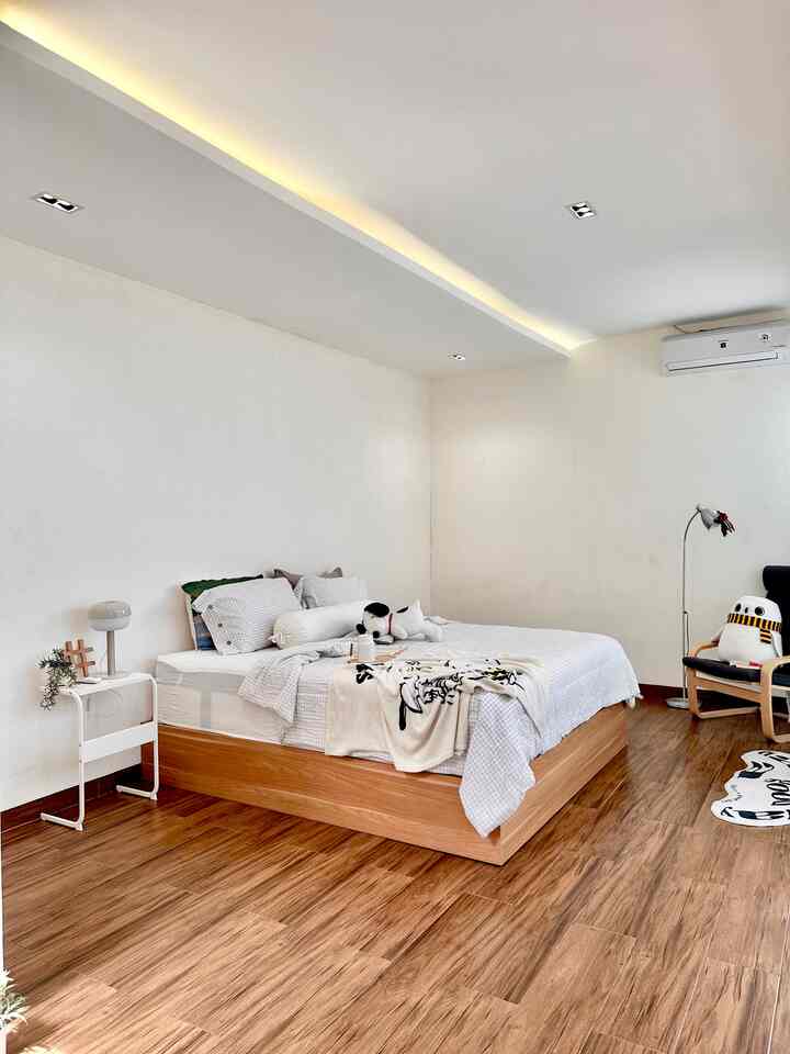 Modern bedroom with white and wood tones, featuring a bed, armchair, and baby products creating a cozy atmosphere