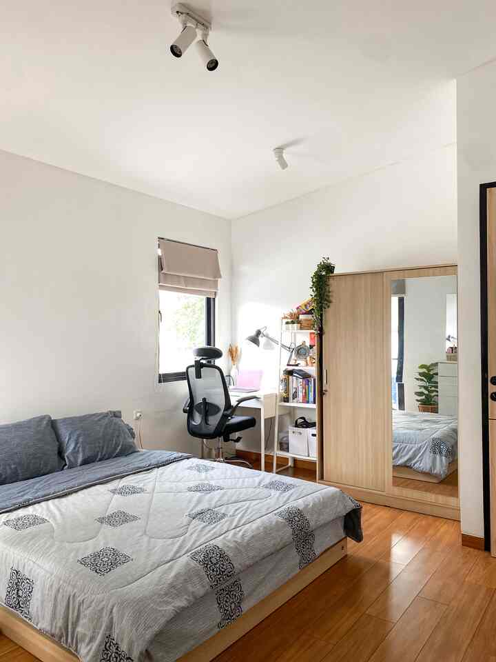 White-walled bedroom with brown wooden floor, featuring wardrobe and desk creating a cozy compact space