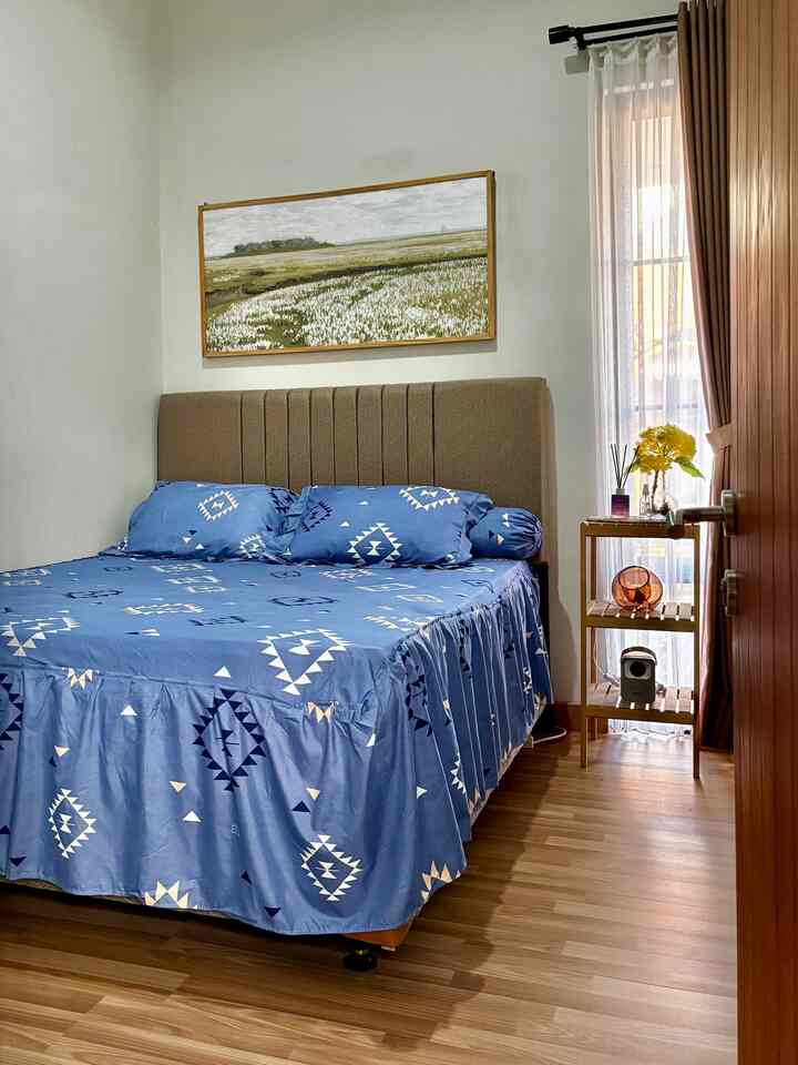 Cozy bedroom featuring brown wood-tone flooring and blue patterned bedding with natural lighting