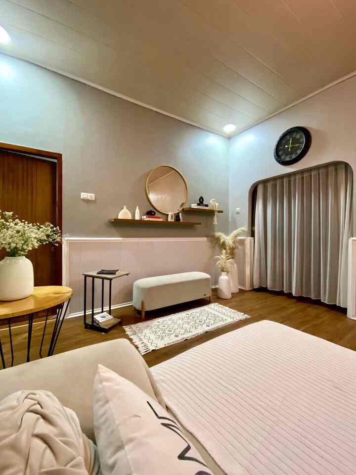 White and brown toned living room corner featuring a stool, patterned rug, and round mirror in a simple natural setting