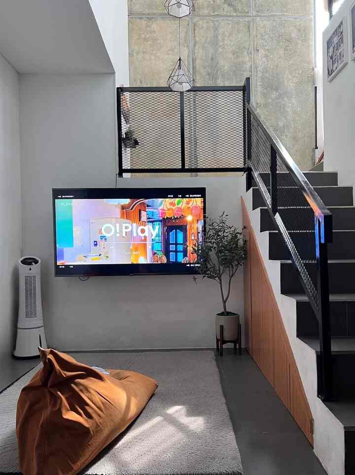 Gray-toned living room featuring wall-mounted TV, brown bean bag, and carpet beside staircase in a modern space