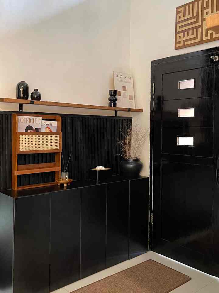 Minimal entrance space featuring black cabinet and door with wooden shelf and decorative items
