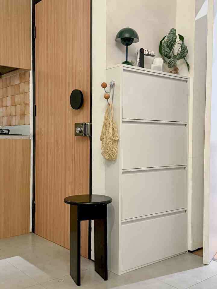 A white and natural-toned entrance featuring a white shoe cabinet and black stool in a neat, minimal style