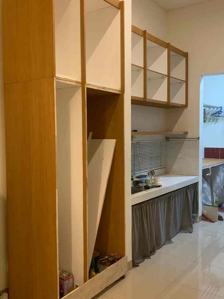 A narrow kitchen space with white walls and wood-toned cabinets, featuring blinds on the window and a clean countertop area