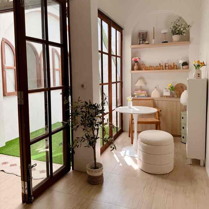 Bright natural wood tone and white open space featuring a small table, stool, plants creating a cozy multifunctional reading area