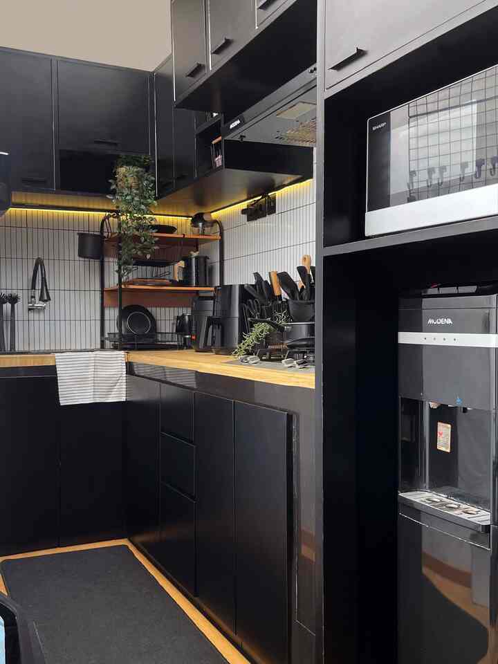 A compact kitchen space dominated by black and wood tones, featuring numerous cabinets and modern appliances organized neatly