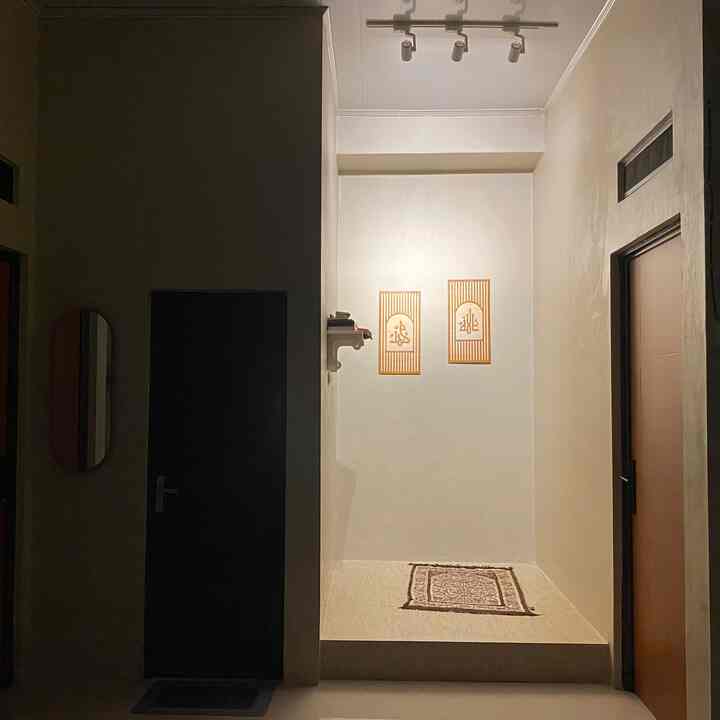 Warm beige toned mihrab space featuring wooden framed calligraphy and small wall shelf in a clean prayer room